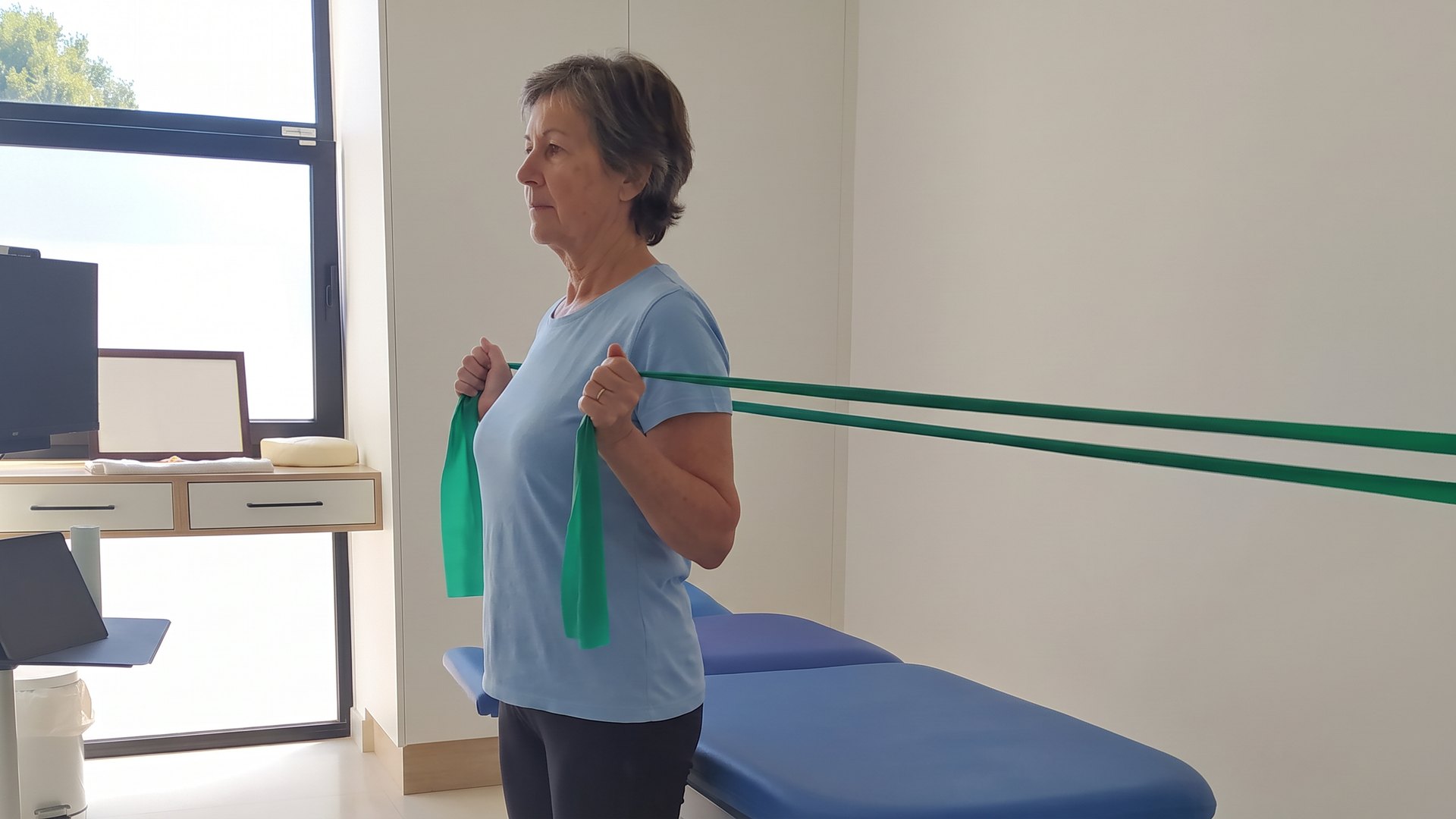 Mujer de unos 60 años haciendo rotación externa de hombro con una banda elástica en la consulta de fisioterapia de Salufit, en Calpe